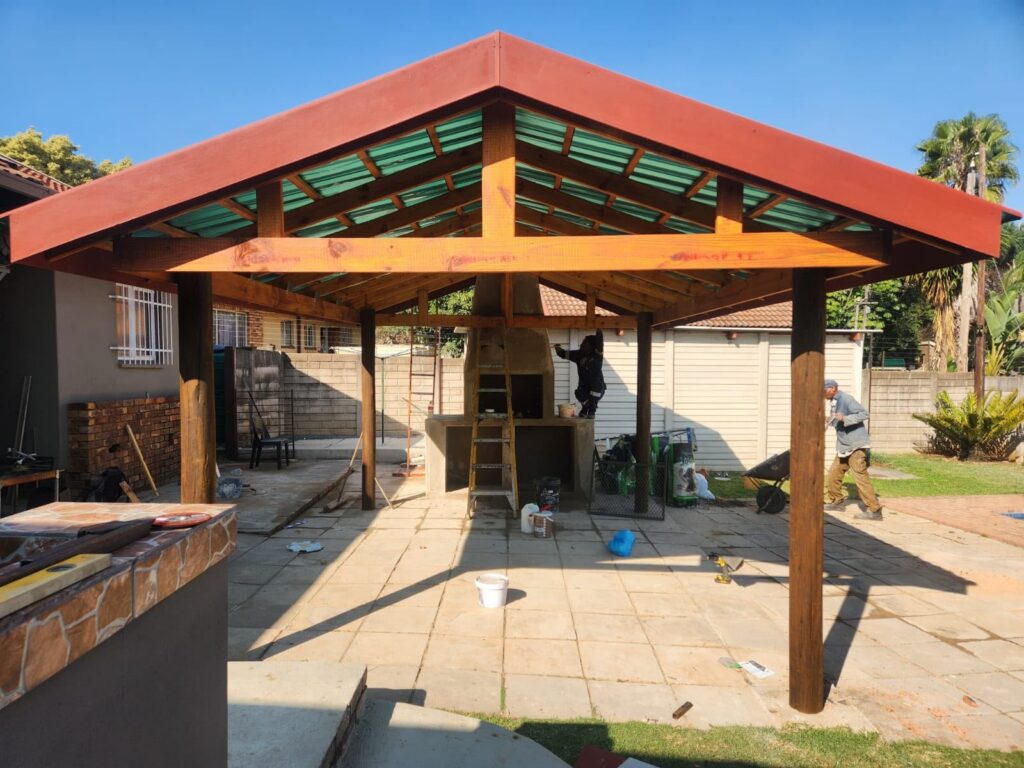 Timber-framed lapa roof under construction over a paved patio